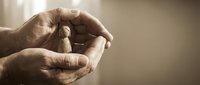 Elderly hands gently cupping and protecting small wooden figurine in warm light symbolizing care, protection, guidance and nurturing relationships.