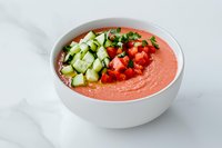 Refreshing gazpacho soup garnished with diced cucumber, tomatoes and herbs in white bowl on marble background. Chilled Spanish summer appetizer.