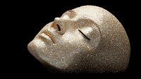 Serene female face covered in gold glitter and sparkles against dark background, eyes closed in peaceful expression, artistic portrait study for makeup and fashion concepts.
