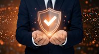 Professional businessman in dark suit holding glowing security shield with checkmark symbol representing protection, trust and verification concepts.