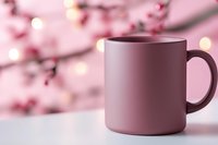 Pink ceramic mug on white surface against blurred spring cherry blossom background with bokeh lights creating cozy atmosphere for lifestyle design.