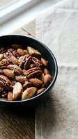 Mixed nuts in black bowl on rustic wooden table with natural lighting for healthy snacking and cooking ingredients.