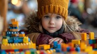 Young Caucasian girl in mustard yellow knit beanie and fur-trimmed winter coat plays with colorful building blocks, capturing childhood wonder against soft bokeh background.