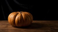 Large orange pumpkin on rustic wooden table against dark background for autumn harvest decoration and seasonal cooking ingredients.