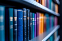 Row of colorful hardcover books arranged on wooden library shelf, with focus on blue volumes in foreground creating depth of field effect. Suitable for education themes.