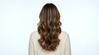 Young woman with long wavy brown hair with blonde highlights viewed from behind wearing cream sweater on white background isolated for design.