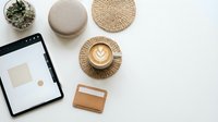Minimalist workspace flatlay with tablet, latte art coffee, woven placemats, leather wallet and succulent plant on white background for modern lifestyle branding.