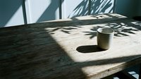 Minimalist workspace with white ceramic mug on wooden table, natural sunlight casting leaf shadows, modern interior design aesthetic for creative projects and lifestyle content.