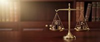 Golden scales of justice on wooden desk in law office with books and warm sunlight creating professional legal atmosphere for attorney services.