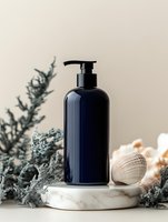 Navy blue cosmetic pump bottle on marble stand with seashells and dried blue coral decorative elements. Minimalist spa composition against beige background.