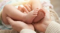 Newborn baby feet resting in parent's hands, tender moment capturing bonding and care. Use for parenting, family, healthcare, and maternity content.
