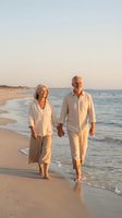 Happy senior couple walking hand in hand on beach at sunset wearing white casual clothing during romantic vacation getaway.
