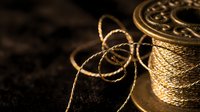 Golden rope cord spools with twisted fibers in warm lighting for crafting and nautical projects on dark textured surface.