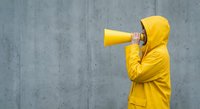 Person in bright yellow raincoat using megaphone against concrete wall for communication and announcement concepts.