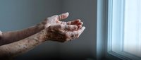 Elderly hands cupped together in prayer or meditation pose near window with soft natural light creating peaceful spiritual moment for healthcare concepts.