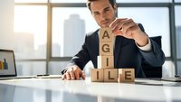 Professional businessman in suit building AGILE word with wooden blocks on modern office desk, representing project management methodology and business strategy.