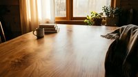 Wooden desk with warm sunlight streaming through window, coffee mug and plants creating productive workspace atmosphere for home office or creative work.
