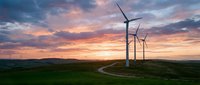 Wind turbines on green hills at sunset with dramatic colorful sky and winding path through renewable energy landscape for sustainable power generation.