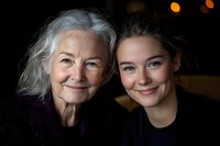 Heartwarming portrait of senior grandmother with silver hair and young adult granddaughter sharing genuine smiles and close bond against dark background.