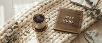 Cozy flat lay with hot coffee cup on chunky knit blanket and letter board saying Stay Home, warm hygge lifestyle concept.
