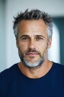 Portrait of mature Caucasian man with gray hair and beard wearing navy blue shirt, looking confidently at camera. Natural lighting creates soft shadows highlighting facial features.
