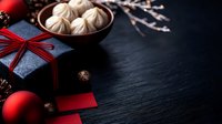 Box, red ribbon, matte baubles and traditional dumplings on dark stone background with copy space.