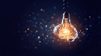 Glowing light bulb with warm filament against dark blue background with golden bokeh particles and sparks for innovation and creativity concepts.
