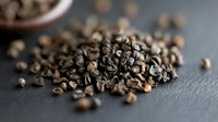 Roasted coffee beans scattered on dark slate surface with selective focus and shallow depth of field, creating artisanal culinary atmosphere.