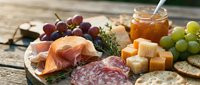 Gourmet charcuterie board with prosciutto, salami, aged cheeses, fresh grapes, honey jar, crackers on rustic wooden surface for entertaining and dining.