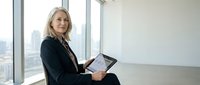 Confident mature businesswoman with tablet in modern office space with city view. Professional executive planning strategy and reviewing data.