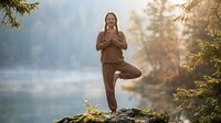 Young woman practicing tree pose yoga meditation outdoors in serene mountain forest setting during golden hour sunrise for mindfulness and wellness.