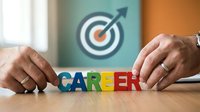 Young adult male professional arranging colorful career letters on wooden desk with target arrow symbol on wall background, representing career planning and professional development goals.