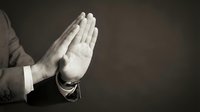 Businessman hands pressed together in prayer gesture against dark background expressing faith, meditation and spiritual contemplation in corporate setting.