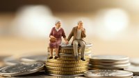 Senior couple sitting on stack of coins representing retirement savings and financial planning for elderly future security and pension fund investment.