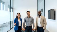 Young diverse professionals in modern office corridor with glass partitions and mounted screen, representing teamwork and corporate collaboration.