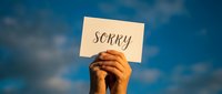 Hands holding a white card with the word Sorry against a blue sky, expressing apology, regret, and sincere emotion in a heartfelt moment.