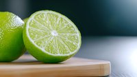 Fresh lime cut in half showing juicy pulp and bright green peel on wooden cutting board against dark background, macro food photography.