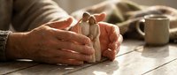 Elderly hands gently holding wooden family figures on rustic table, symbolizing care, protection and family bonds in warm natural lighting.