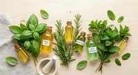Fresh herbs and essential oils arranged on neutral background with mortar and pestle for natural wellness and aromatherapy applications.