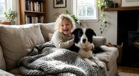 Young blonde toddler girl cuddling with black and white border collie dog on beige sofa in cozy living room with books and fireplace for family lifestyle.