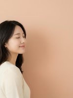 Young East Asian woman with long black hair wearing cream sweater, eyes closed in peaceful expression against warm beige background, suitable for wellness and lifestyle content.