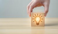 Hand holding wooden cube with glowing lightbulb icon representing innovation, creativity, and bright ideas for business solutions and brainstorming concepts.