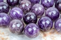 Natural amethyst crystal spheres showing deep purple color variations and translucent properties on light marble surface, macro photography of mineral gemstones.
