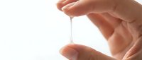 Closeup of hand holding liquid droplet suspended between fingers against white background, representing skincare, cosmetics, serum, or medical treatment application.
