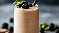 Creamy smoothie topped with fresh blackberries and mint leaves, served in a tall glass with a straw for breakfast or healthy beverage recipes.