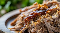 Slow cooked pulled pork with barbecue sauce on white plate ready for sandwiches and meals. Tender shredded meat with caramelized glaze for comfort food recipes.
