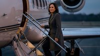 Professional businesswoman in dark suit boarding private jet aircraft at airport terminal during evening hours.