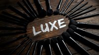 Luxury makeup brushes arranged in circle around wooden sign with luxe text on dark surface for cosmetics and beauty industry.