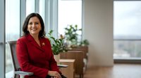 Professional businesswoman in red blazer smiling confidently in modern office with large windows and natural light for corporate presentations.