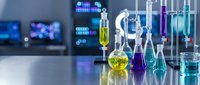 Modern laboratory with colorful chemical solutions in glass flasks and beakers on white table with blurred scientific equipment background.